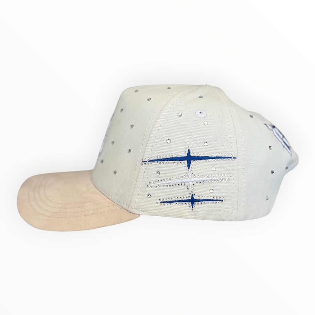 Hype Block white baseball cap with scattered rhinestones, beige suede brim, and blue embroidered side graphic detail.