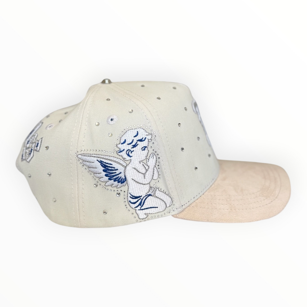 Hype Block white baseball cap with rhinestone accents, beige suede brim, and blue cherub embroidery on the side.