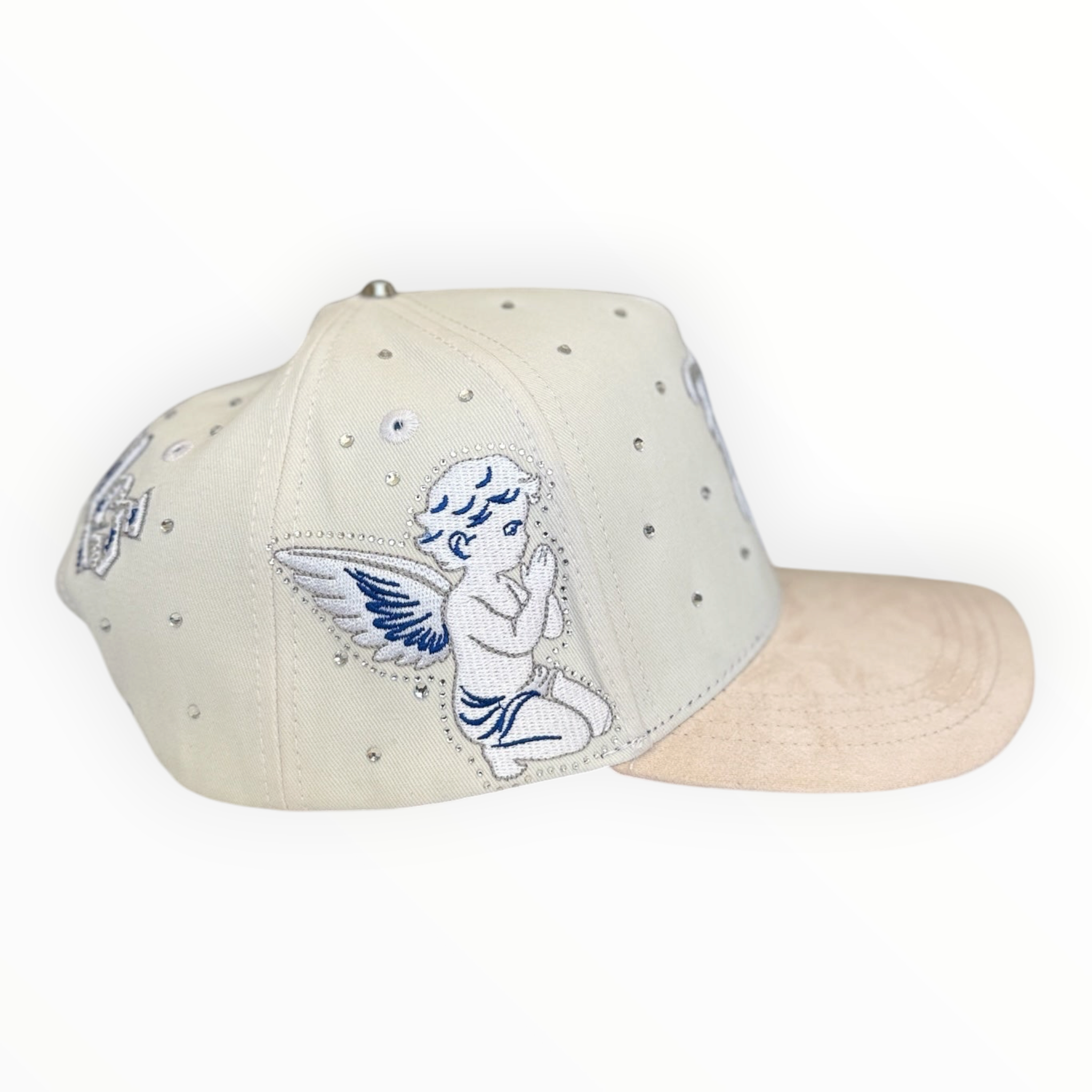 Hype Block white baseball cap with rhinestone accents, beige suede brim, and blue cherub embroidery on the side.