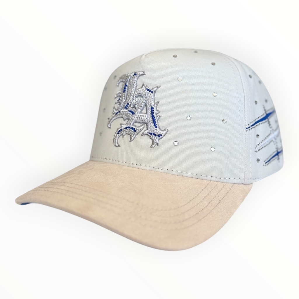 Hype Block white baseball cap with rhinestone LA logo, blue embroidery, and a beige suede-feel brim.